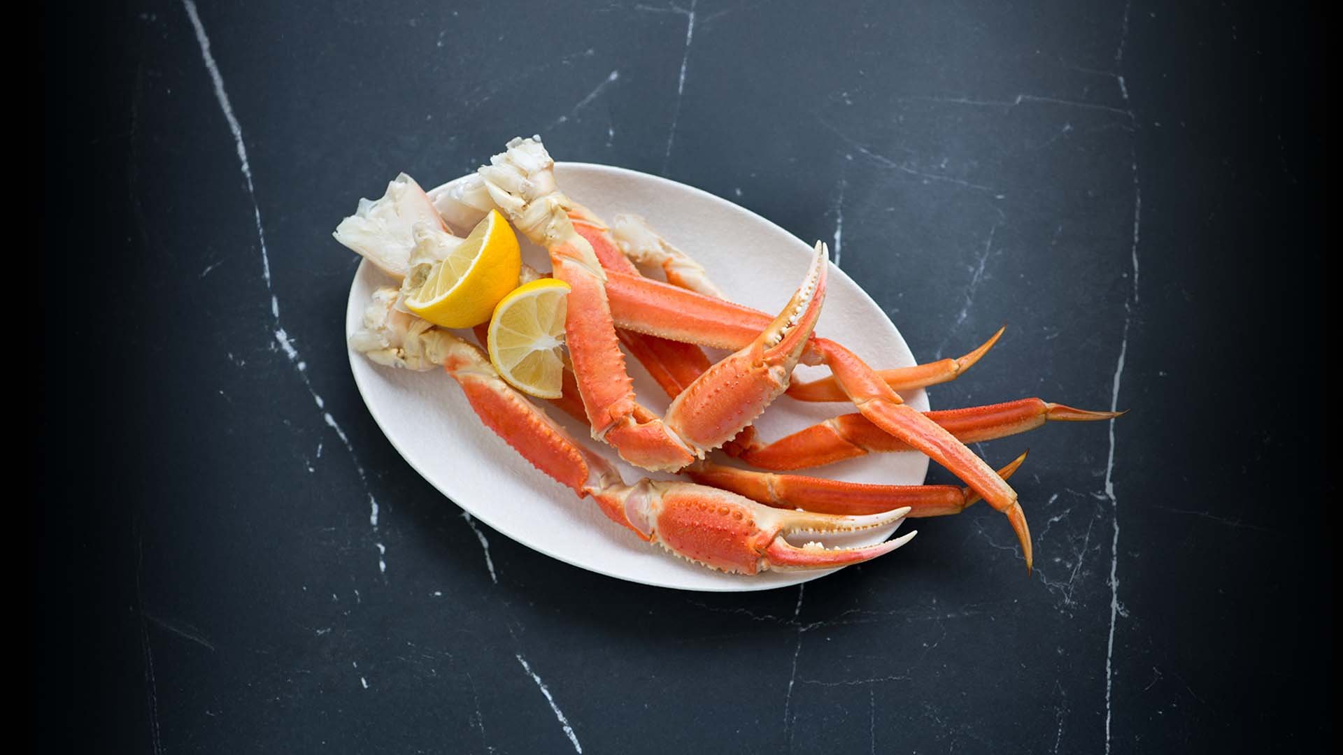 A large white ceramic plate is filled with a colorful and appetizing crab legs with lemon.