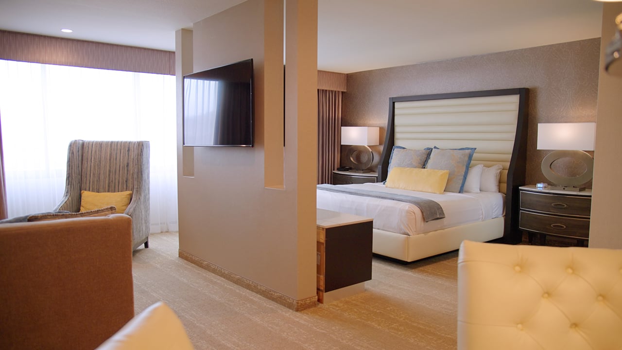 A hotel room with a bed, chair, TV, and window.