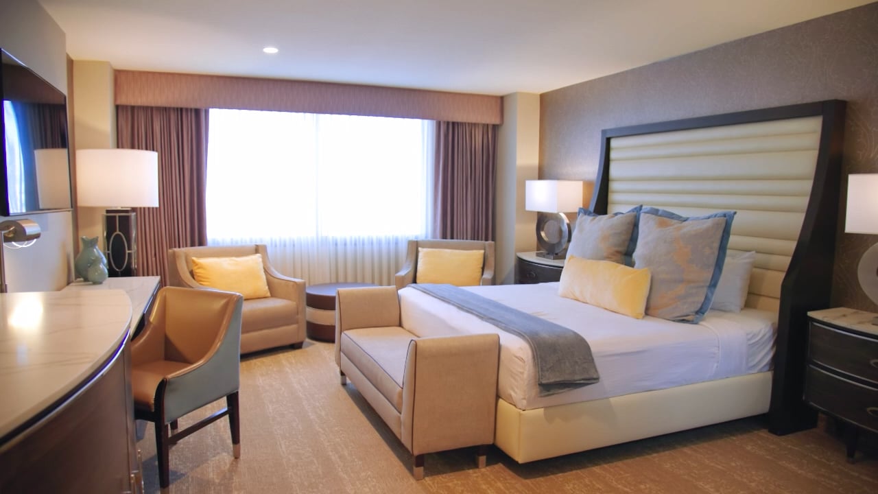 A hotel room with a king-sized bed, desk, seating area, and window.