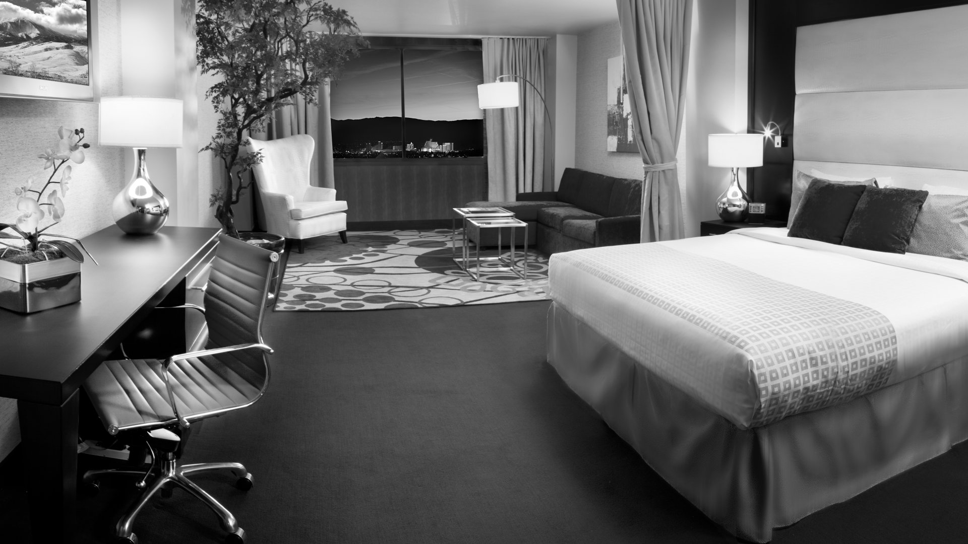 A wide view of a hotel room with a large bed, desk, sofa, and city view.