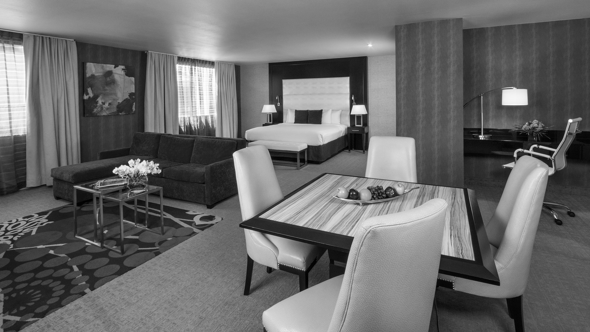 A wide view of a hotel suite with a living area, dining table, and bedroom.