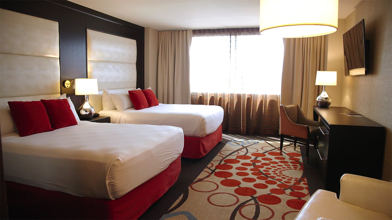 A hotel room with two queen beds, a desk, and a window
