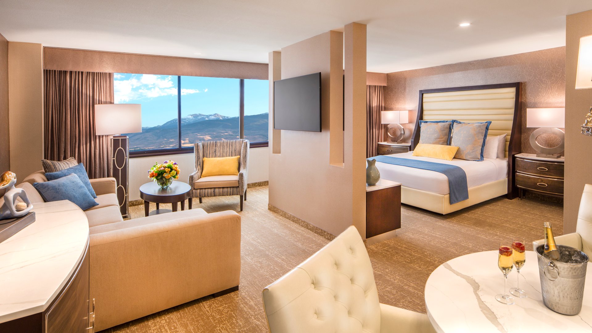 A wide view of a hotel suite with a sitting area, bed, and mountain view.