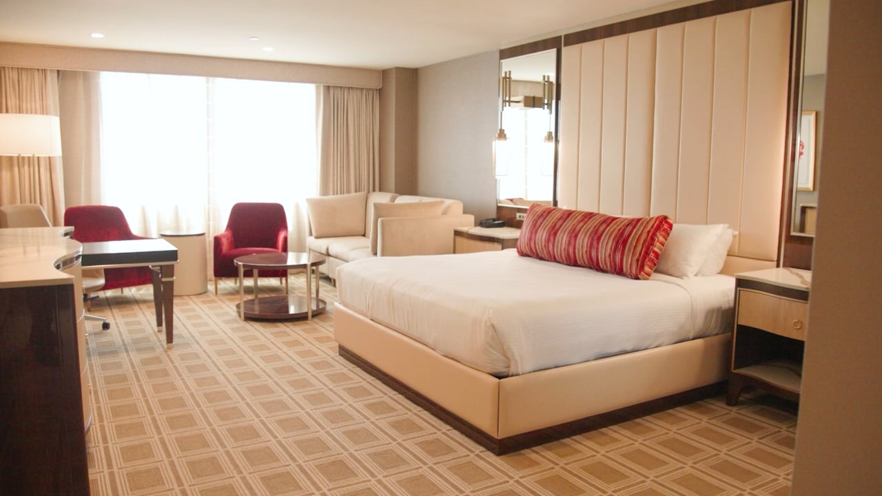 A hotel room with a king-sized bed, sitting area, and large window.