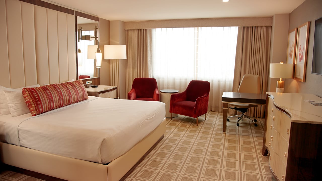 A hotel room with a large bed, desk, chairs, and a window.