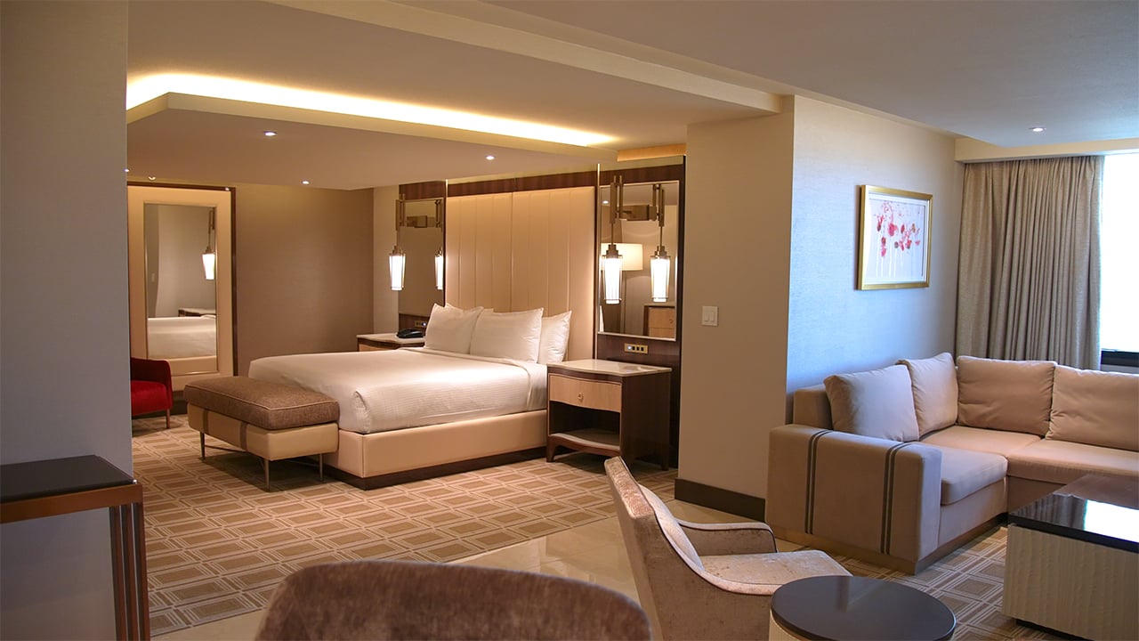 A wide view of a hotel suite with a bed, sofa, coffee table, and chair.